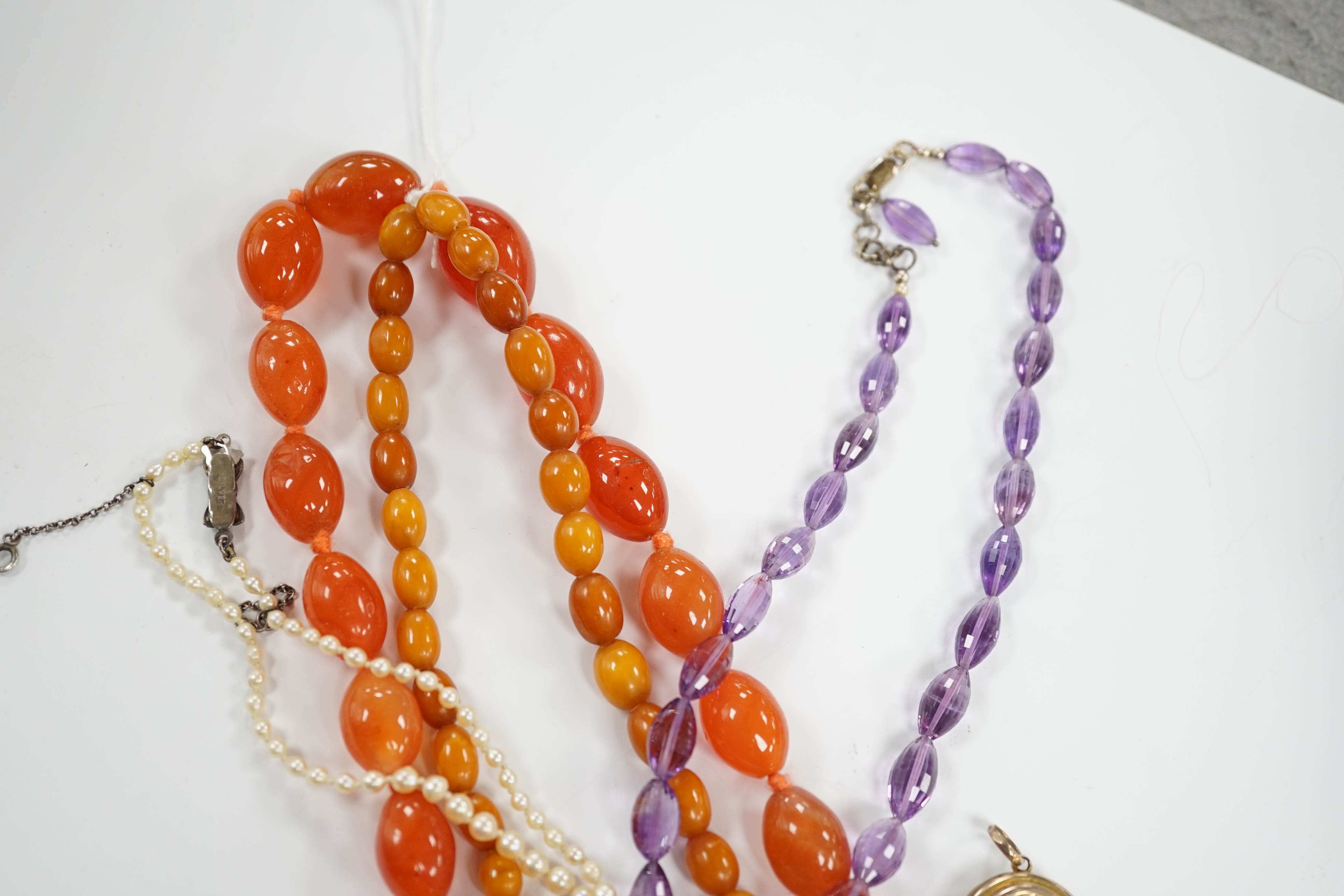 A gold plated oval locket and four assorted single strand necklaces including cultured pearl, amber, agate and amethyst.